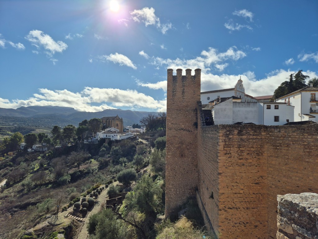 Remnants of the old defensive walls of Ronda. Sweeping views open across the countryside, dotted with white houses and rolling hills stretching far into the distance.