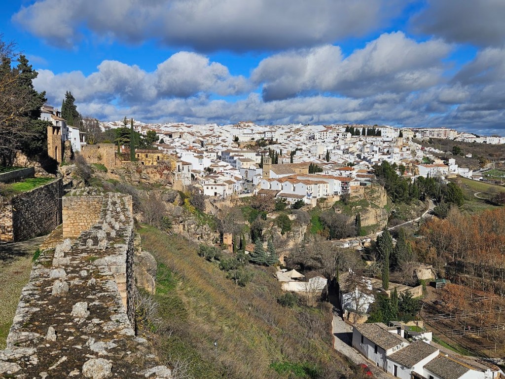 Remnants of the old defensive walls of Ronda. Sweeping views open across the countryside, dotted with white houses and rolling hills stretching far into the distance.